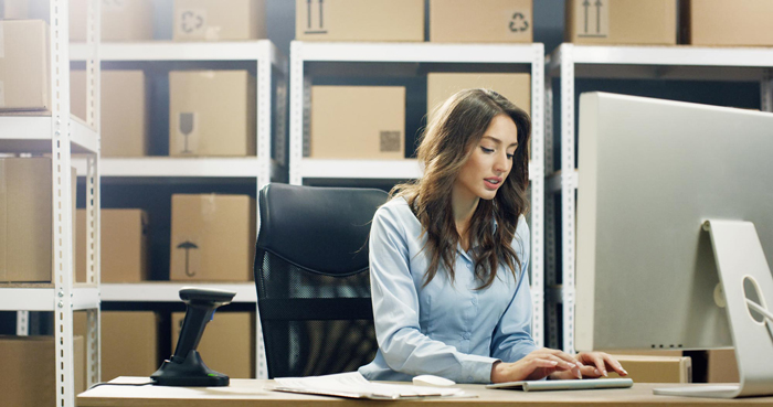 female postal worker working at computer in post delivery office and typing on keyboard